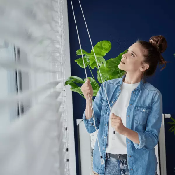 femme qui manoeuvre un store vénitien blanc à l'aide d'une manoeuvre cordon